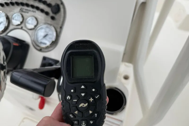 Slide: The Image of Hand holding a remote control on a 2020 Carolina Skiff 21 LS boat dashboard. - 55