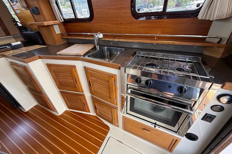 Slide: The Image of 2020 Ranger Tugs R-31 CB galley with stove, sink, and wooden cabinetry. - 15