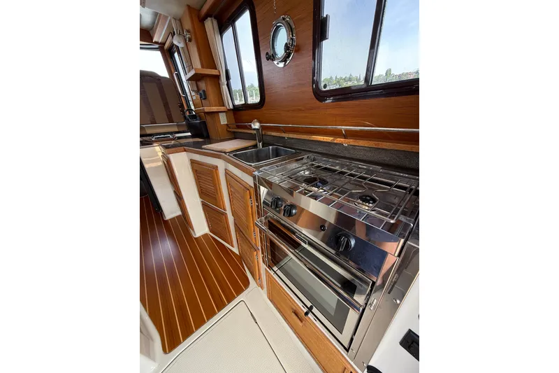 Slide: The Image of 2020 Ranger Tugs R-31 CB galley with stove, sink, and wooden cabinetry. - 16