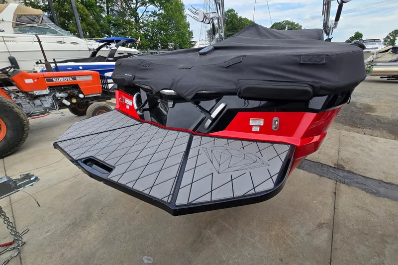 Slide: The Image of 2019 MasterCraft XT25 boat with covered stern, parked near other boats and equipment. - 12