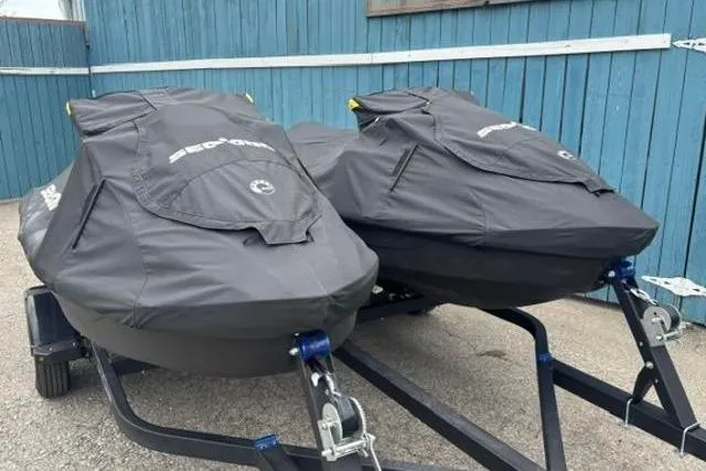 Slide: The Image of Two covered 2021 Seadoo GTI SE 130 jet skis on a trailer, parked by a blue wall. - 21