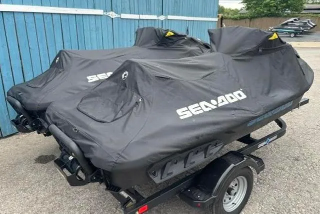 Slide: The Image of 2021 Seadoo GTI SE 130 jet skis covered on a trailer, parked by a blue fence. - 22