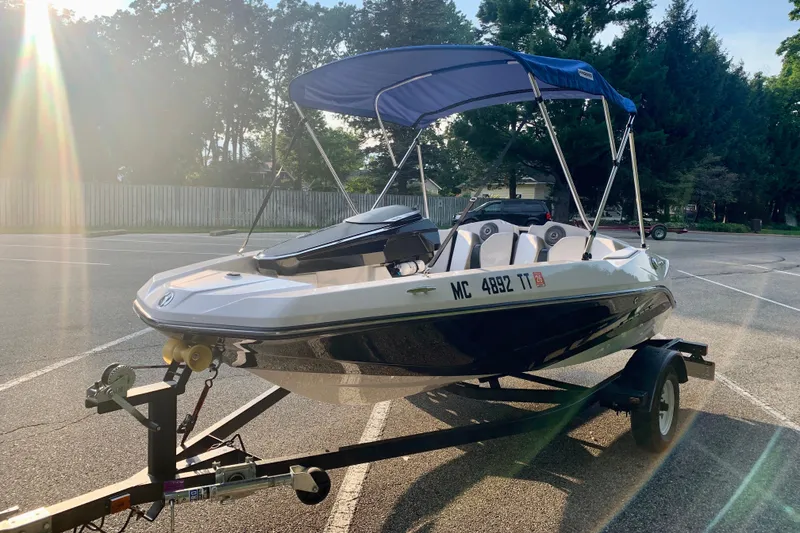 The Image of 2015 Scarab 165 ID boat on trailer with blue canopy in sunny parking lot. - 0
