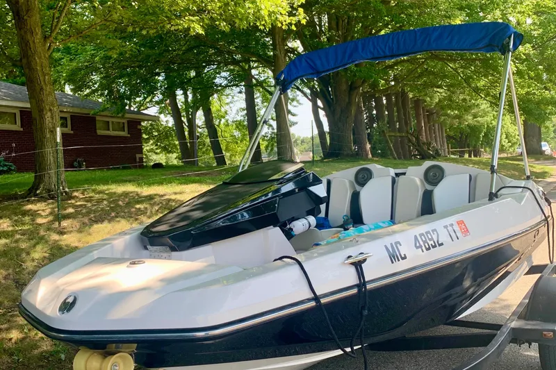 Slide: The Image of 2015 Scarab 165 ID boat with blue canopy, parked on a trailer under trees. - 5