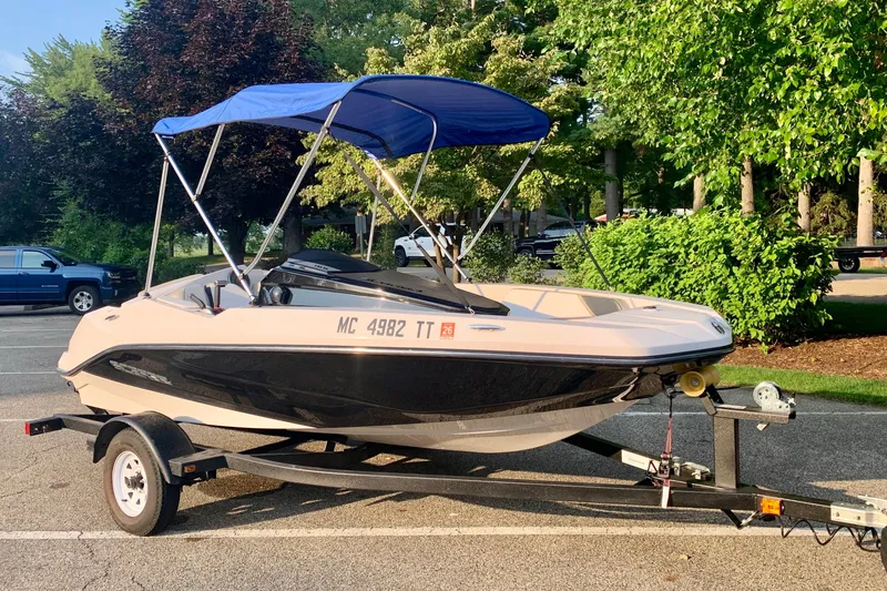 Slide: The Image of 2015 Scarab 165 ID boat with blue canopy on trailer in parking lot. - 6