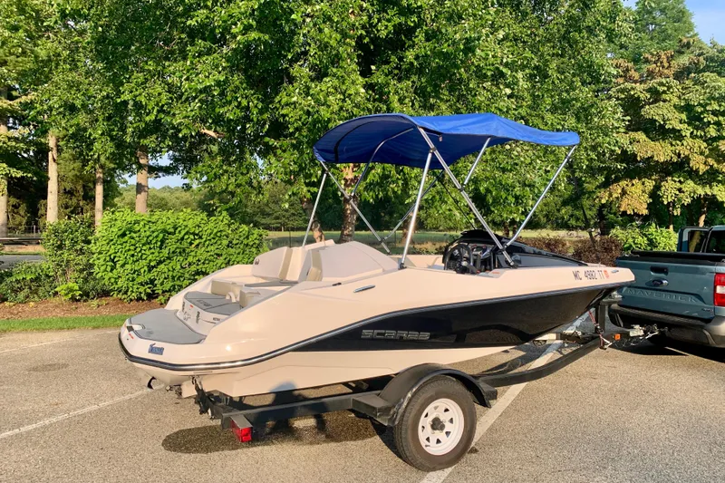 Slide: The Image of 2015 Scarab 165 ID boat with blue canopy on trailer, parked near lush greenery. - 7