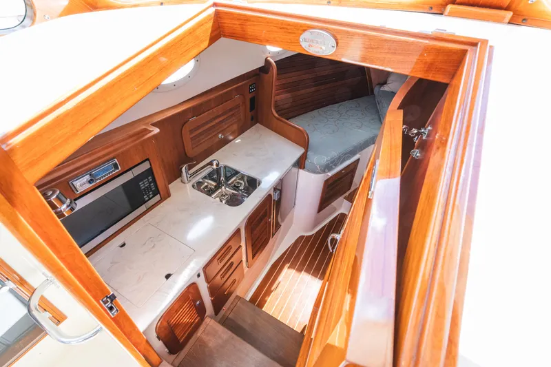 Slide: The Image of Hinckley Talaria 34 interior, featuring a compact kitchen with wood cabinetry and a cozy sleeping area. - 29