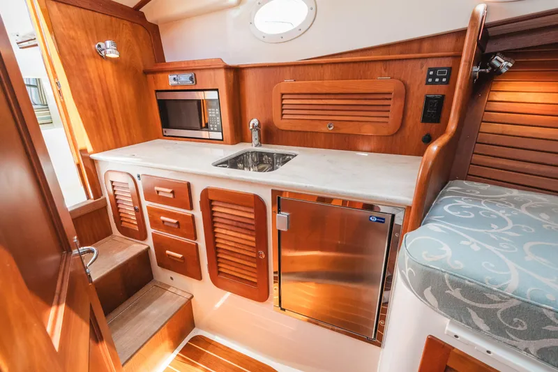 Slide: The Image of Hinckley Talaria 34 yacht interior, featuring a compact kitchen with wood cabinetry and modern appliances. - 32