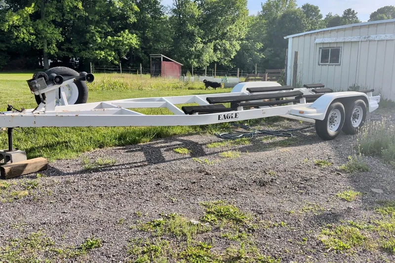 Slide: The Image of White boat trailer on gravel, surrounded by greenery, near a metal building. - 23