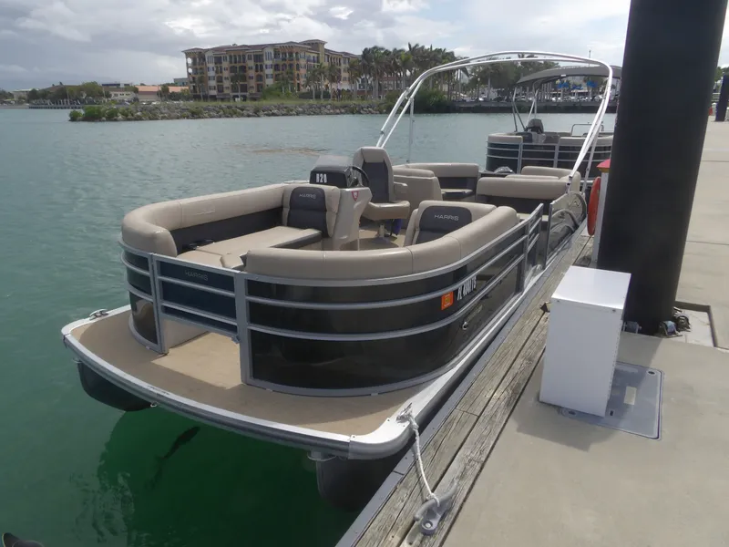 Slide: The Image of 2024 Harris Pontoon boat docked with water in the background. - 21