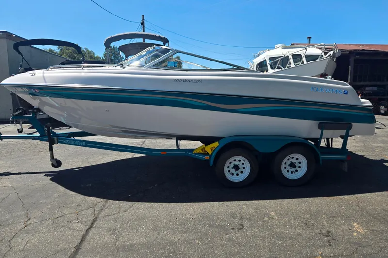 Slide: The Image of 1996 Four Winns 200 Horizon boat on trailer, white with teal accents, parked outdoors. - 3