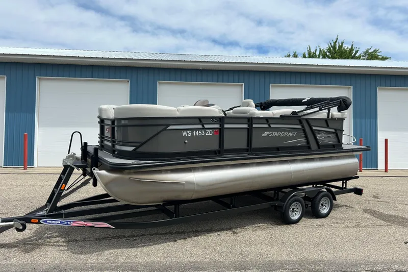 Slide: The Image of 2022 Starcraft CX 21 C pontoon boat on trailer, parked near blue building. - 12