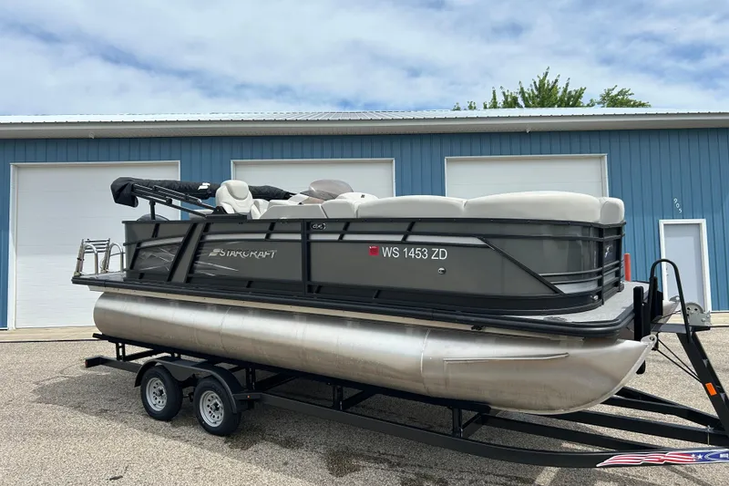 Slide: The Image of 2022 Starcraft CX 21 C pontoon boat on trailer, parked outside blue building. - 2