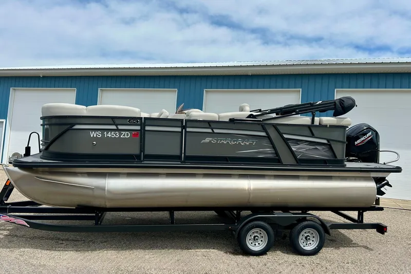 Slide: The Image of 2022 Starcraft CX 21 C pontoon boat on trailer, parked outside a blue building. - 3