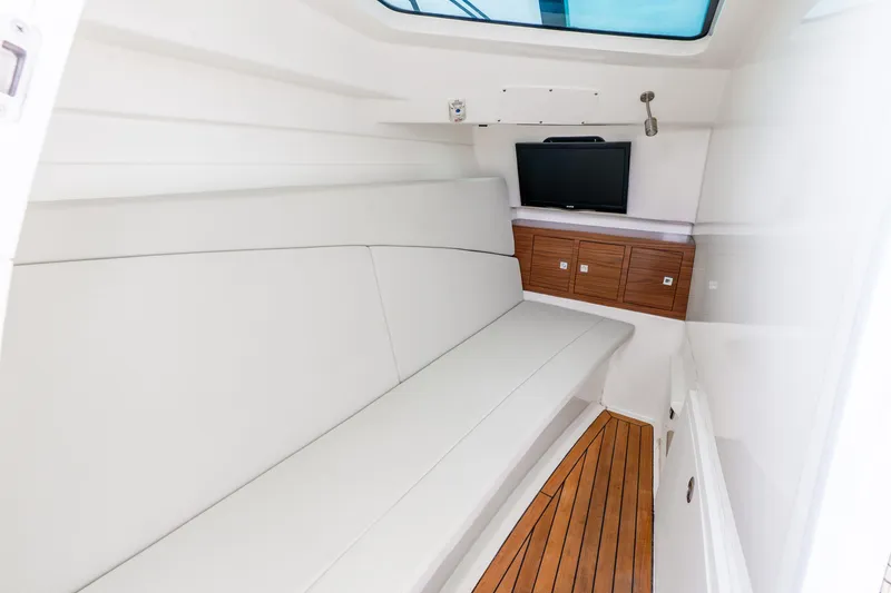 Slide: The Image of 2017 Boston Whaler 320 Vantage cabin interior with white seating, wood flooring, and TV. - 43