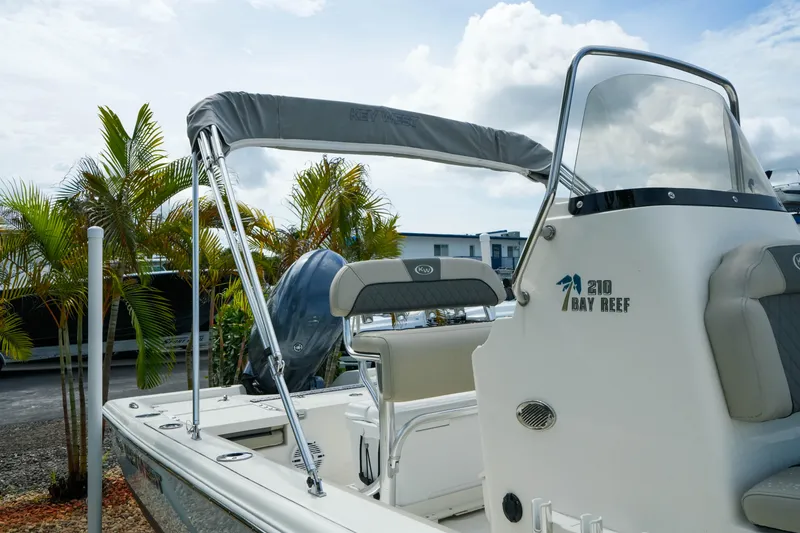 Slide: The Image of 2025 Key West 210 Bay Reef boat with canopy, parked near tropical plants. - 12