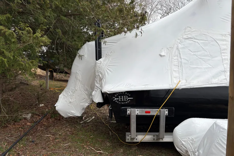 Slide: The Image of 2020 Hells Bay Ester boat covered in protective white wrap, parked outdoors near trees. - 3