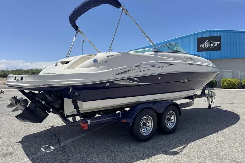 Slide: The Image of 2005 Sea Ray 220 Sundeck boat on trailer, parked near a blue building. - 10