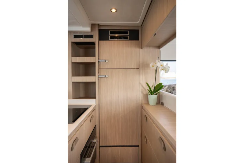 Slide: The Image of Modern yacht kitchen interior with wooden cabinetry, built-in appliances, and a potted orchid. Prestige F4.9, 2025. - 20