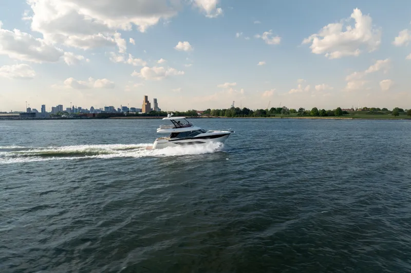 Slide: The Image of A 2025 Prestige F4.9 yacht cruising on a sunny day with city skyline in background. - 6