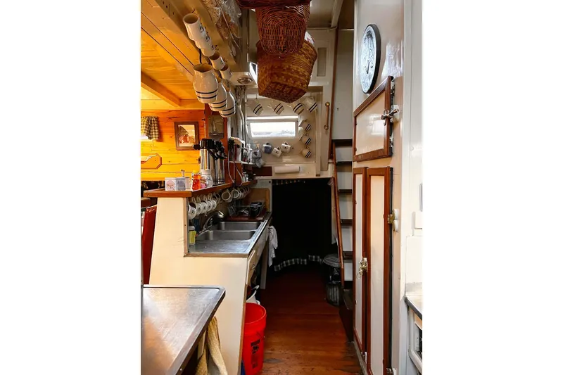 Slide: The Image of Interior of a 1962 Classic Coasting Schooner kitchen with wooden accents and hanging mugs. - 12