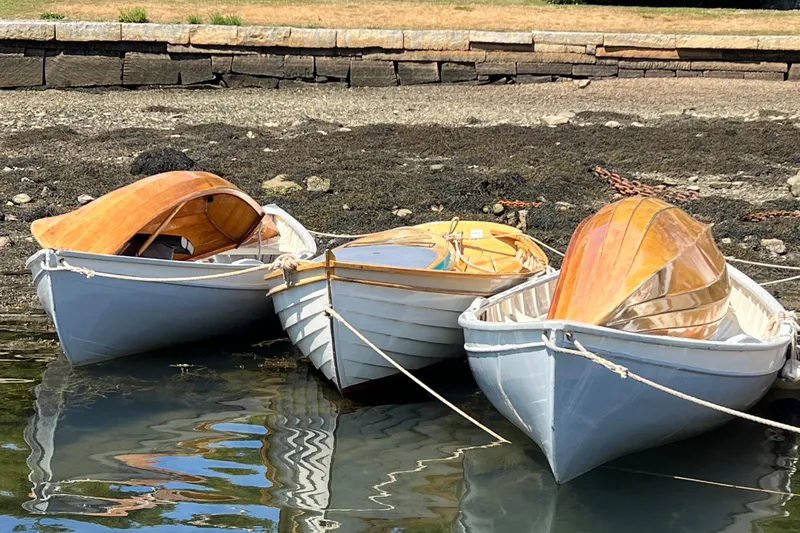 Slide: The Image of Three classic wooden boats docked by a stone wall, reflecting in calm water. - 18