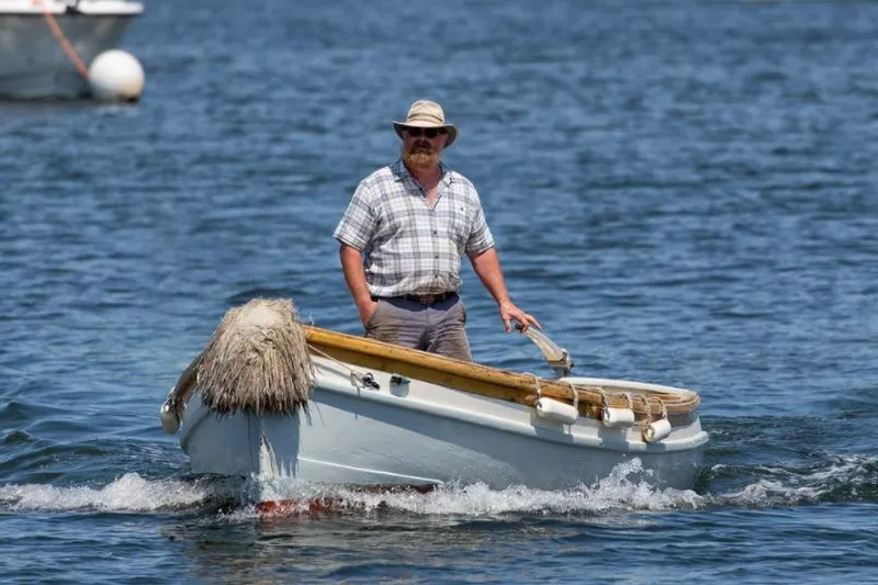 Slide: The Image of Man steering a small boat on water, wearing a hat and plaid shirt. - 19