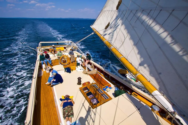 Slide: The Image of Classic 1962 Coasting Schooner sailing with passengers relaxing on deck under clear blue skies. - 4