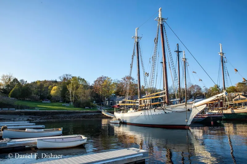 Slide: The Image of Classic 1962 Coasting Schooner docked in a serene harbor under a clear blue sky. - 6