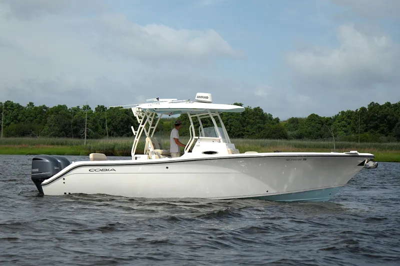 The Image of 2016 Cobia 296 Center Console boat on water, with lush green shoreline in background. - 0