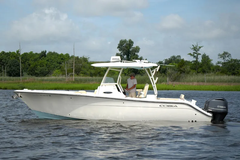 Slide: The Image of 2016 Cobia 296 Center Console boat cruising on a calm river with lush greenery. - 2