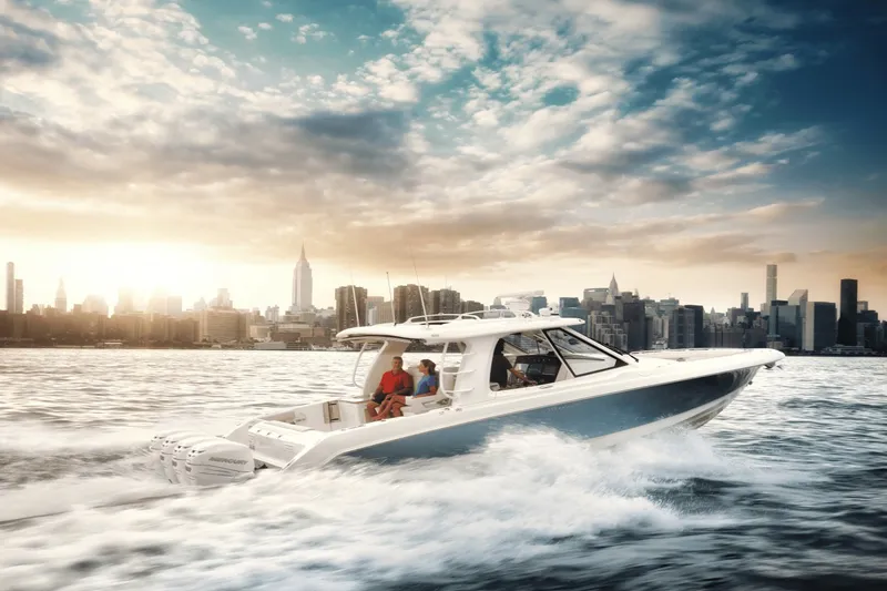 Slide: The Image of A 2027 Boston Whaler 380 Realm cruising through water at sunset with a city skyline backdrop. - 38