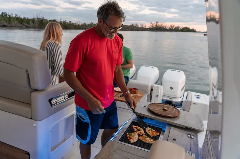 Slide: The Image of A man grills pizza on a boat with two people standing in the background. It's evening. - 21