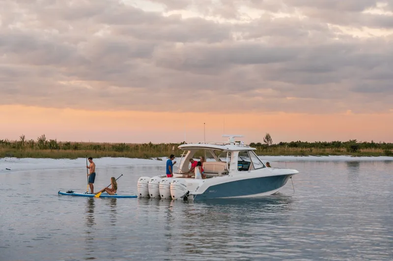 Slide: The Image of A 2027 Boston Whaler 380 Realm on calm water at sunset, with people on paddleboards. - 15