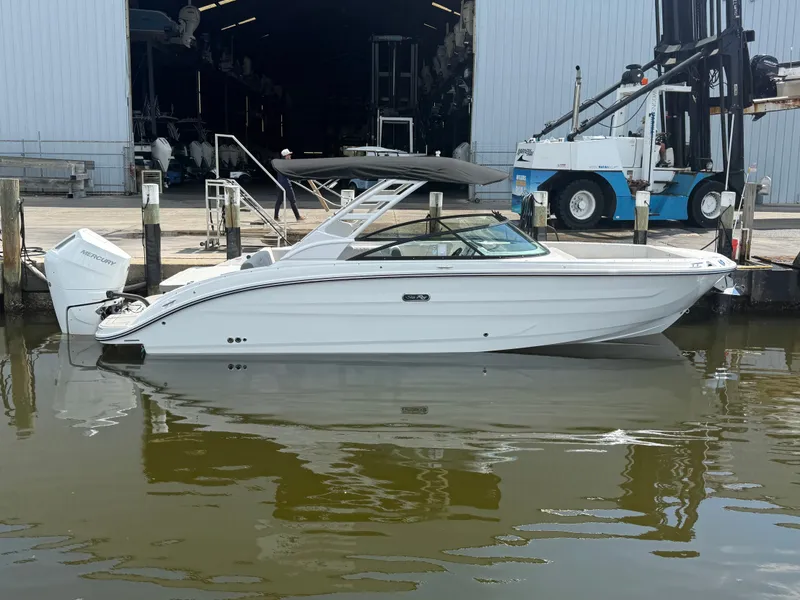 Slide: The Image of A white 2027 Sea Ray SDX 270 Outboard boat is docked in the water near a warehouse. - 1