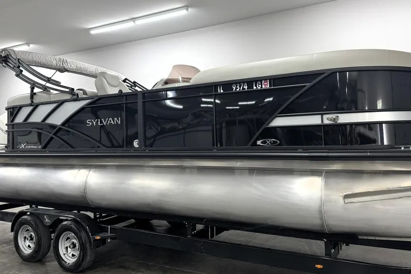 Slide: The Image of 2025 Sylvan Mirage X X5 pontoon boat on trailer in indoor storage. - 2