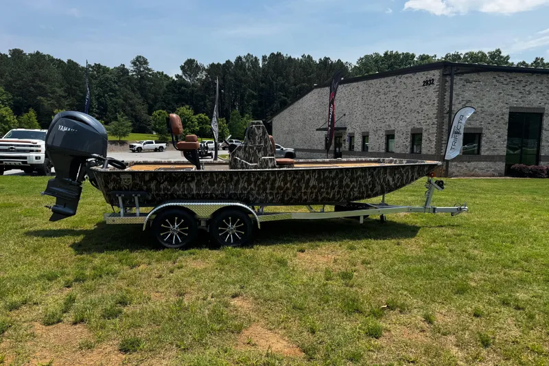 Slide: The Image of 2026 Avid 207 Recon boat on trailer, camo design, parked on grass near building. - 21