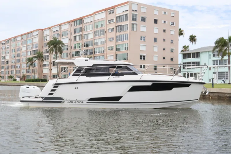 Slide: The Image of 2024 Aquador 300 HT yacht cruising near waterfront buildings. - 2