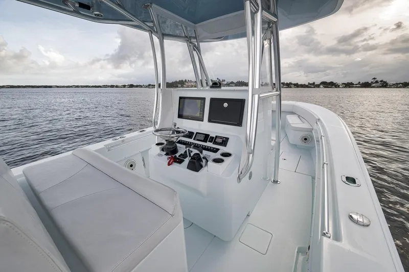 Slide: The Image of 2019 Contender 32 ST boat interior with helm, steering wheel, and navigation screens on calm water. - 68