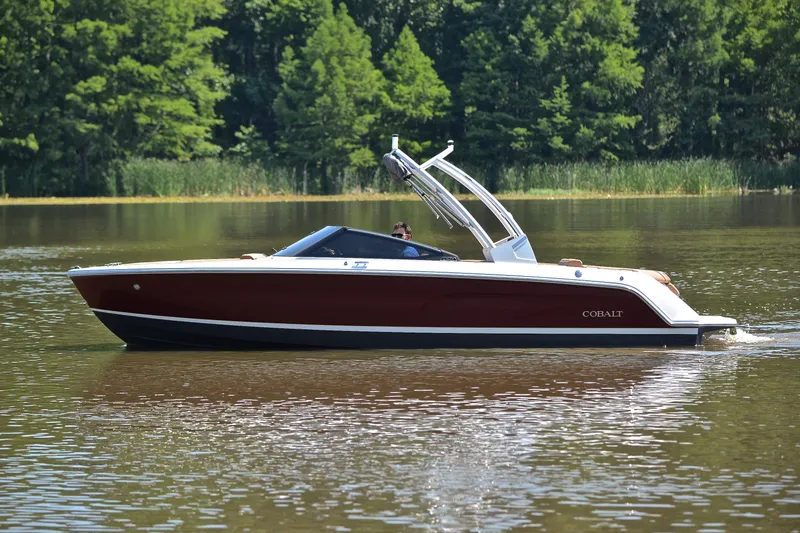 Slide: The Image of 2024 Cobalt CS23 boat cruising on a serene lake with lush green trees. - 10
