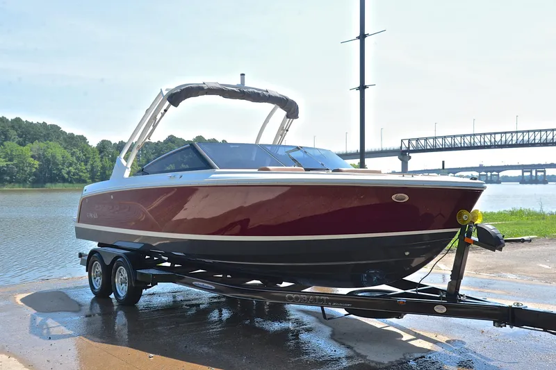 Slide: The Image of 2024 Cobalt CS23 boat on trailer by river, bridge in background. - 17