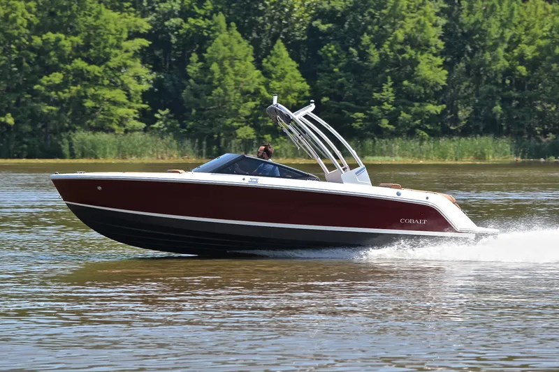 Slide: The Image of 2024 Cobalt CS23 boat cruising on a lake with lush green trees in the background. - 2