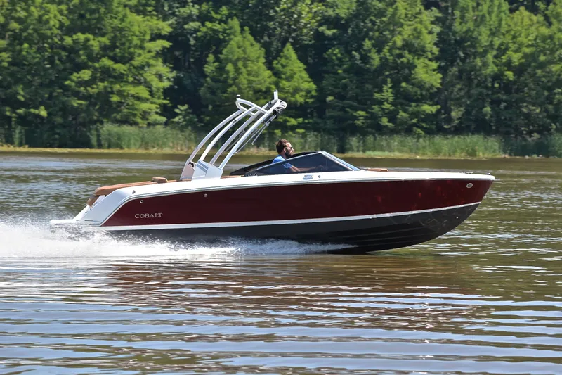Slide: The Image of 2024 Cobalt CS23 boat cruising on a lake with lush green trees in the background. - 3
