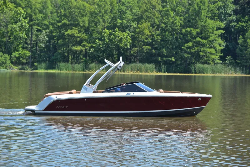 Slide: The Image of 2024 Cobalt CS23 boat cruising on a serene lake with lush green trees. - 8