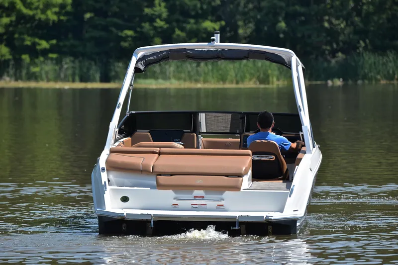 Slide: The Image of 2024 Cobalt CS23 boat cruising on a calm lake with lush greenery. - 9