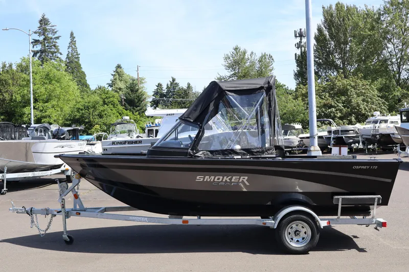 Slide: The Image of 2026 Smoker Craft Osprey 172 boat on trailer, parked outdoors with trees in background. - 2