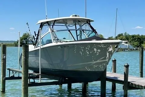 Slide: The Image of 2024 Cobia 280 Dual Console boat docked on a lift in a serene marina. - 10