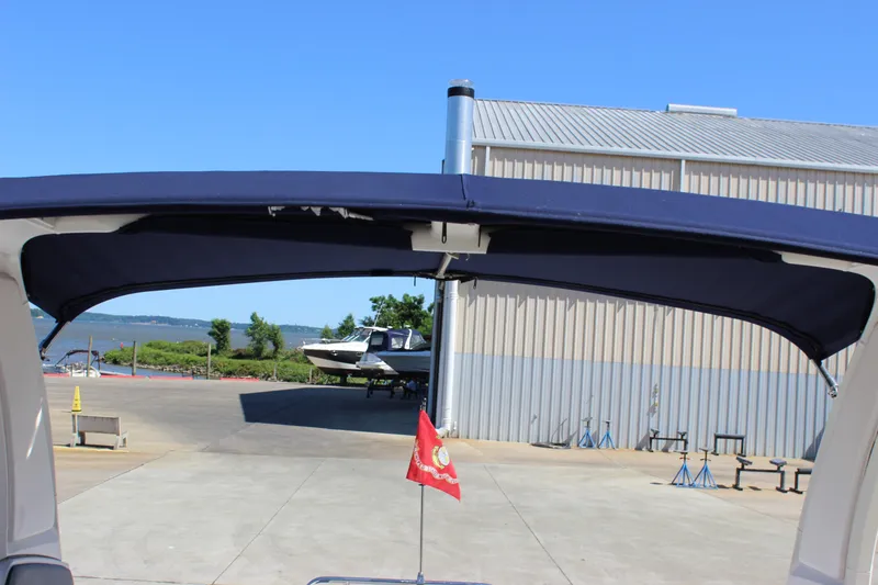 Slide: The Image of 2020 Chaparral 277 SSX boat with navy canopy and red flag, docked near a warehouse. - 20