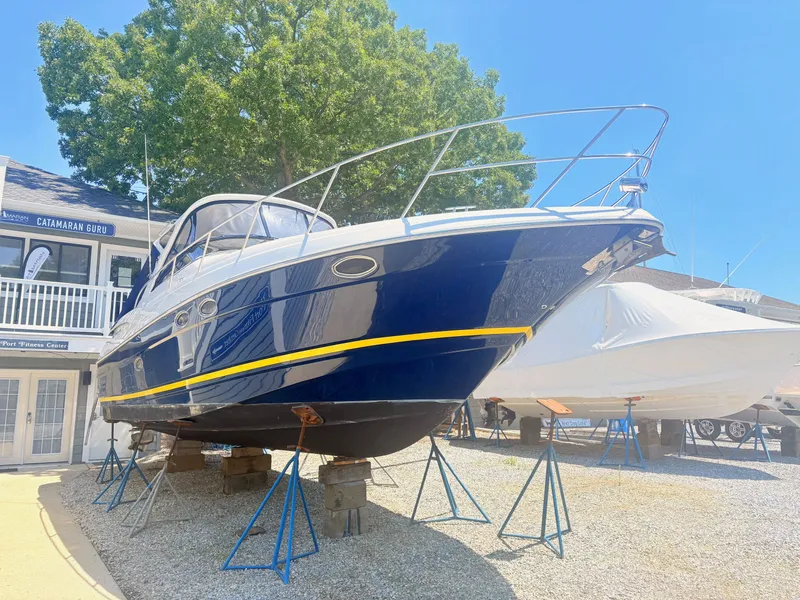 Slide: The Image of A 2009 Regal Commodore 3760 IO is on stands in an outdoor storage area. The hull is blue with yellow accents. - 1