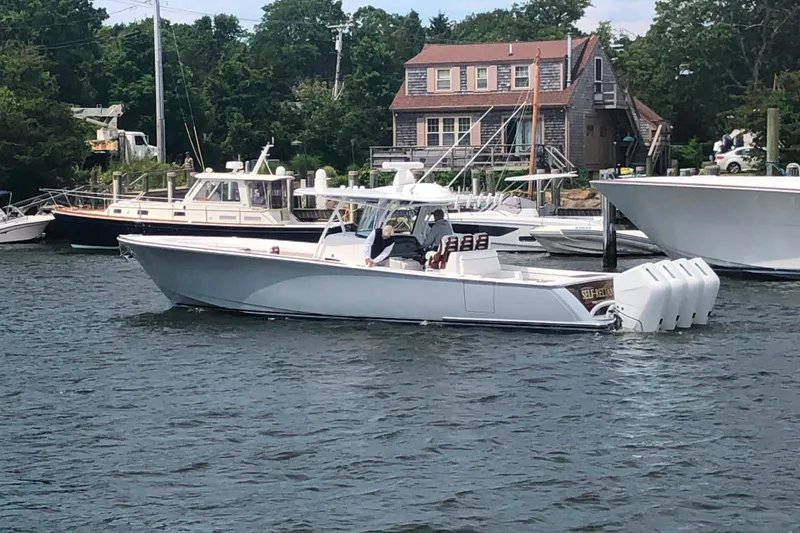 Slide: The Image of 2025 Valhalla Boatworks V-41 cruising on a scenic waterway near docked boats and a rustic house. - 2